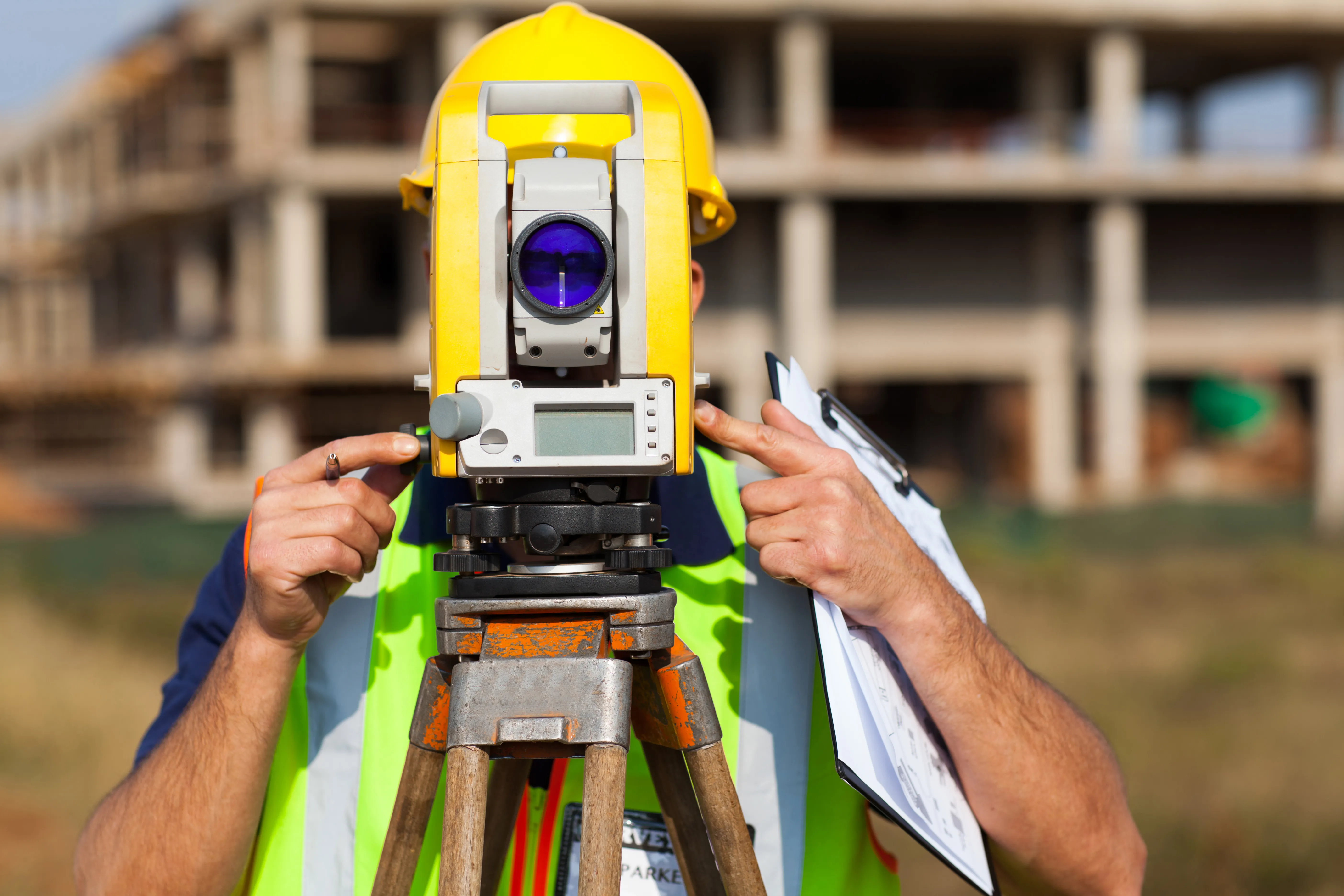 Land surveyor looking through theodolite at construction site